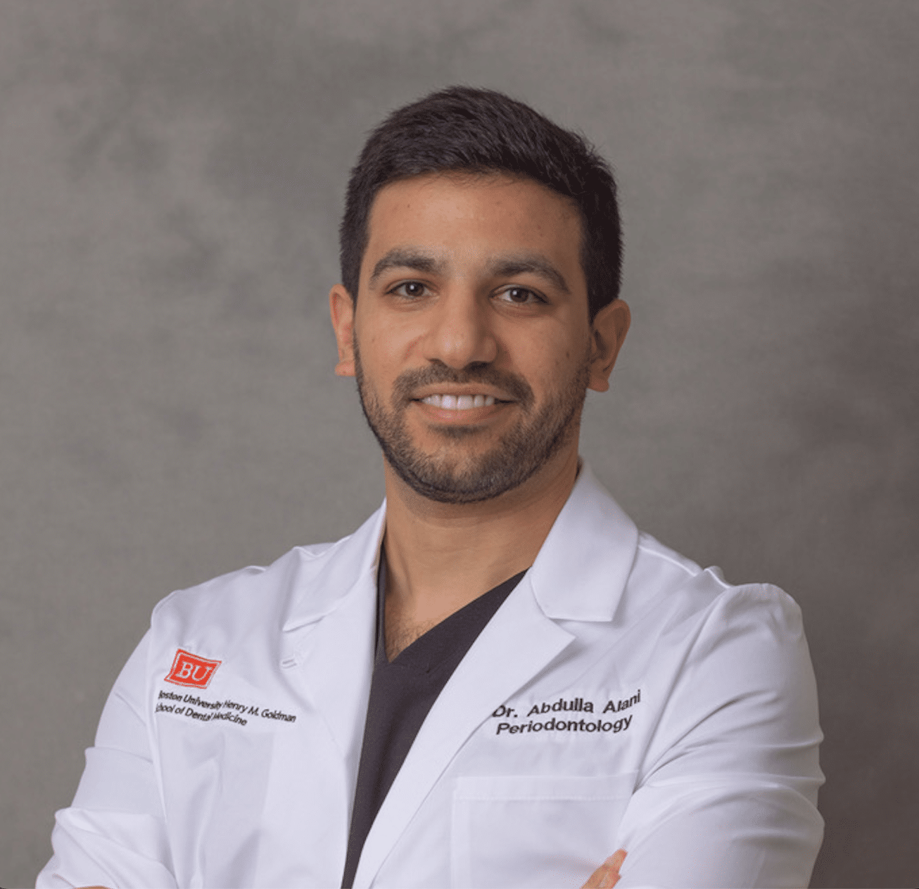Portrait of a smiling male dentist in a white coat with a name tag reading Dr. Abdullla Alami, Periodontology, in a professional studio setting.